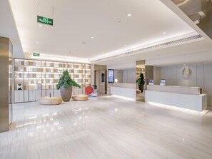 A modern hotel lobby with a reception desk, a large potted plant, and a wall-mounted digital screen.