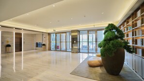 A spacious lobby with a large potted tree, a reception desk, and a glass door entrance.