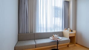 A modern hotel room with a grey sofa, a small round table with a tray, and a wooden desk.