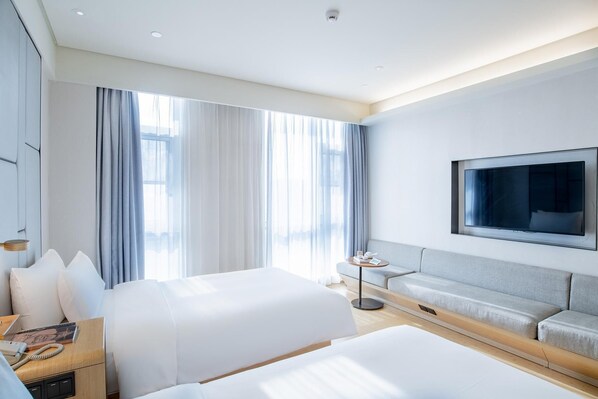 A modern hotel room with two beds, a TV, and a sofa.