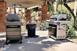 A barbecue grill and a water dispenser in an outdoor area with a concrete floor, surrounded by a fence and greenery. - Sparkling Pool*Corner Unit*Walk Everywhere* (Scottsdale)