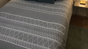 Ein ordentlich bezogenes Bett mit einem gemusterten Überwurf, zwei Kissen und je einer Nachttischlampe auf Holz-Nachttischen.