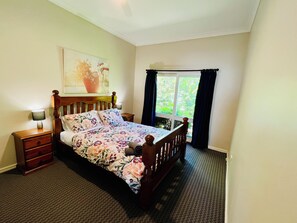 Een slaapkamer met een bed, nachtkastje, lamp, raam met gordijnen en een schilderij aan de muur.