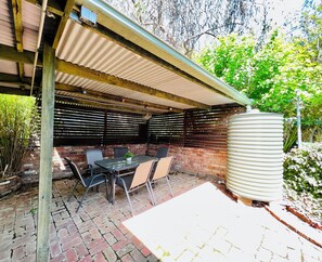 Een terras buiten met een tafel en stoelen, een golfplaten dak en een bakstenen muur.