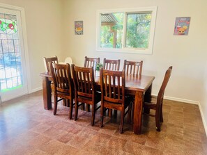 A dining area with a wooden table and chairs, a window with a view of greenery, and a door with a stained glass design. - Treetops Escape   *   Close to CBD   *   Nature   *   Unlimited WIFI (West Albury)