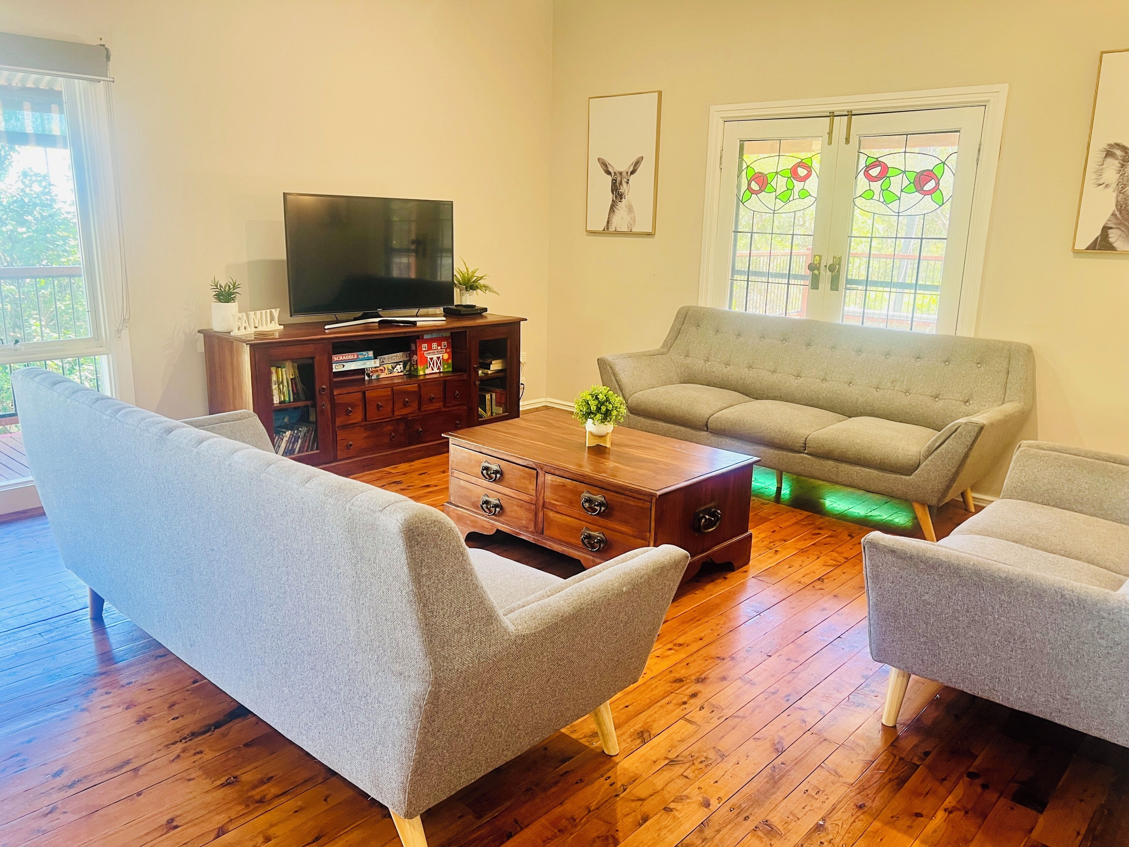 A living room with a sofa, two armchairs, a wooden coffee table, a TV on a stand, and a bookshelf.