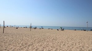 Ein weiter Sandstrand mit Sonnenschirmen und Menschen.
