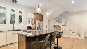 Eine moderne Küche mit einer zentralen Kochinsel, Barhocker und einer Treppe, die zu einem Erker führt.