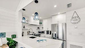Une cuisine moderne avec des meubles blancs, des appareils en acier inoxydable et un grand îlot central doté de tabourets.