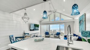 Une cuisine moderne dotée d’un grand îlot central, de meubles blancs et d’appareils électroménagers en acier inoxydable. On y trouve des chaises bleues et une table à manger agrémentée d’un élément décoratif.