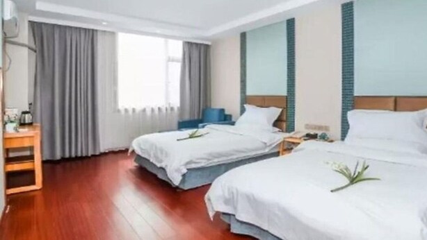 Ein Hotelzimmer mit zwei Betten, Holzboden, Schreibtisch mit Stuhl und einem Vorhangfenster.