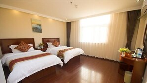 Ein Hotelzimmer mit zwei Betten, einem Schreibtisch, einem Stuhl, einer kleinen Mülltonne und einem Fenster mit Vorhängen.