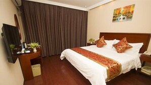 Ein Hotelzimmer mit einem großen Bett, einem Holzkopfteil, einem Flachbildfernseher, einem Schreibtisch mit Pflanze und einem Vorhang.