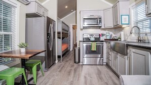 Eine kleine Küche mit Kühlschrank, Mikrowelle, Backofen und Spüle. Es gibt eine kleine Essecke mit Tisch und Stühlen.