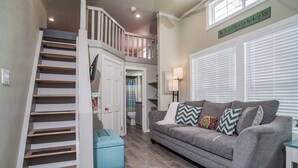 A living room with a grey sofa, teal ottoman, and a staircase with white railings. - River Escape / Fishing Dock / Kayak / FastWiFi (Seguin)