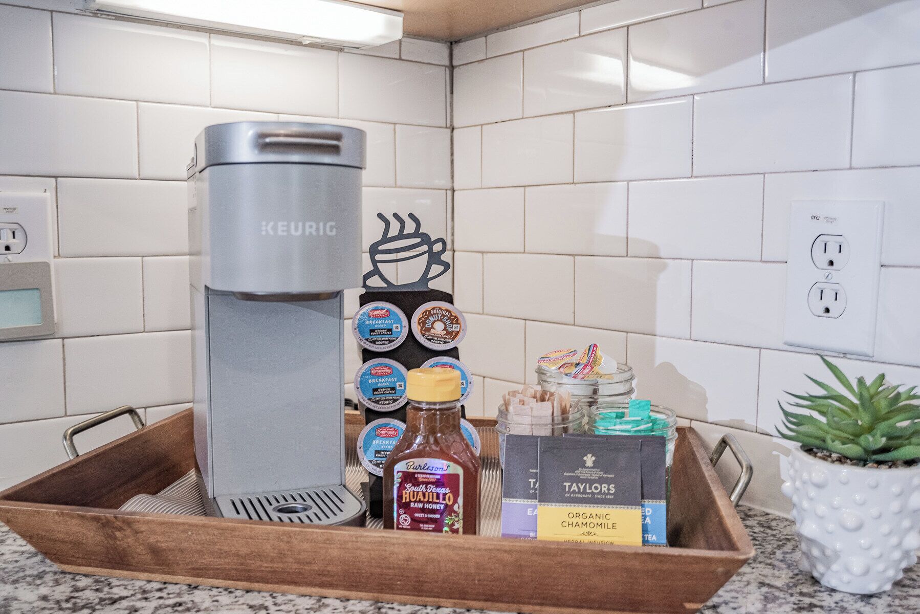 Una cucina con una macchina da caffè Keurig, un vassoio con prodotti per la colazione e una pianta in vaso.