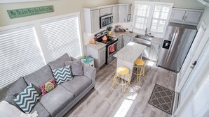 A compact kitchen with a gray sofa, yellow stools, and a small dining area. - River Escape / Fishing Dock / Kayak / FastWiFi (Seguin)