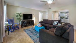A living room with a TV, a ceiling fan, a blue rocking chair, a brown sofa, and a kitchen in the background. - Lakefront Escape / Fishing / Kayaks / Fast WiFi (Seguin)