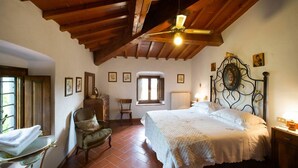 Une chambre avec un plafond en bois, un lit recouvert d’une courtepointe blanche, une chaise, une commode et une fenêtre donnant sur un paysage agréable.