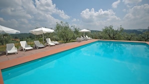 A swimming pool with white lounge chairs and umbrellas, surrounded by trees and a view of hills. - Le Vasche 4 - Apartment with pool (Romola)