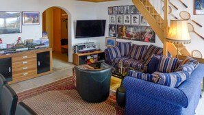 A living room with a high wooden ceiling, a TV, a sofa, and a staircase.