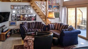 A spacious living room with a large sofa, a television, and a staircase leading to an upper level.