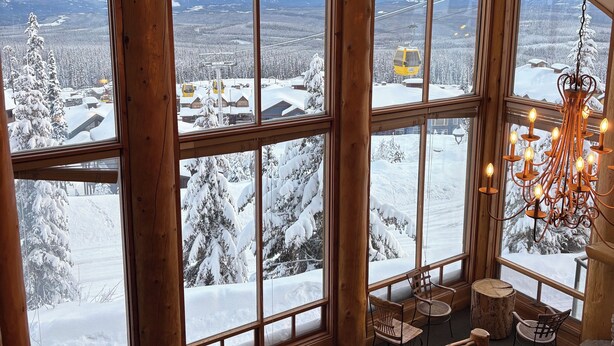 Una cabana acollidora amb grans finestres que donen vista a una muntanya nevada.