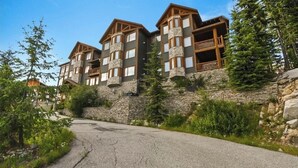 A multi-story lodge with stone walls and wooden balconies, set against a backdrop of trees and a clear sky.