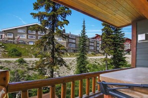 A balcony with a wooden railing overlooking a building with multiple windows and a view of trees and a road.