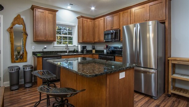 A kitchen with wooden cabinets, stainless steel appliances, a granite countertop, and a bar stool. - BK's Hideaway, with fire-pit and bike storage (Pisgah Forest)