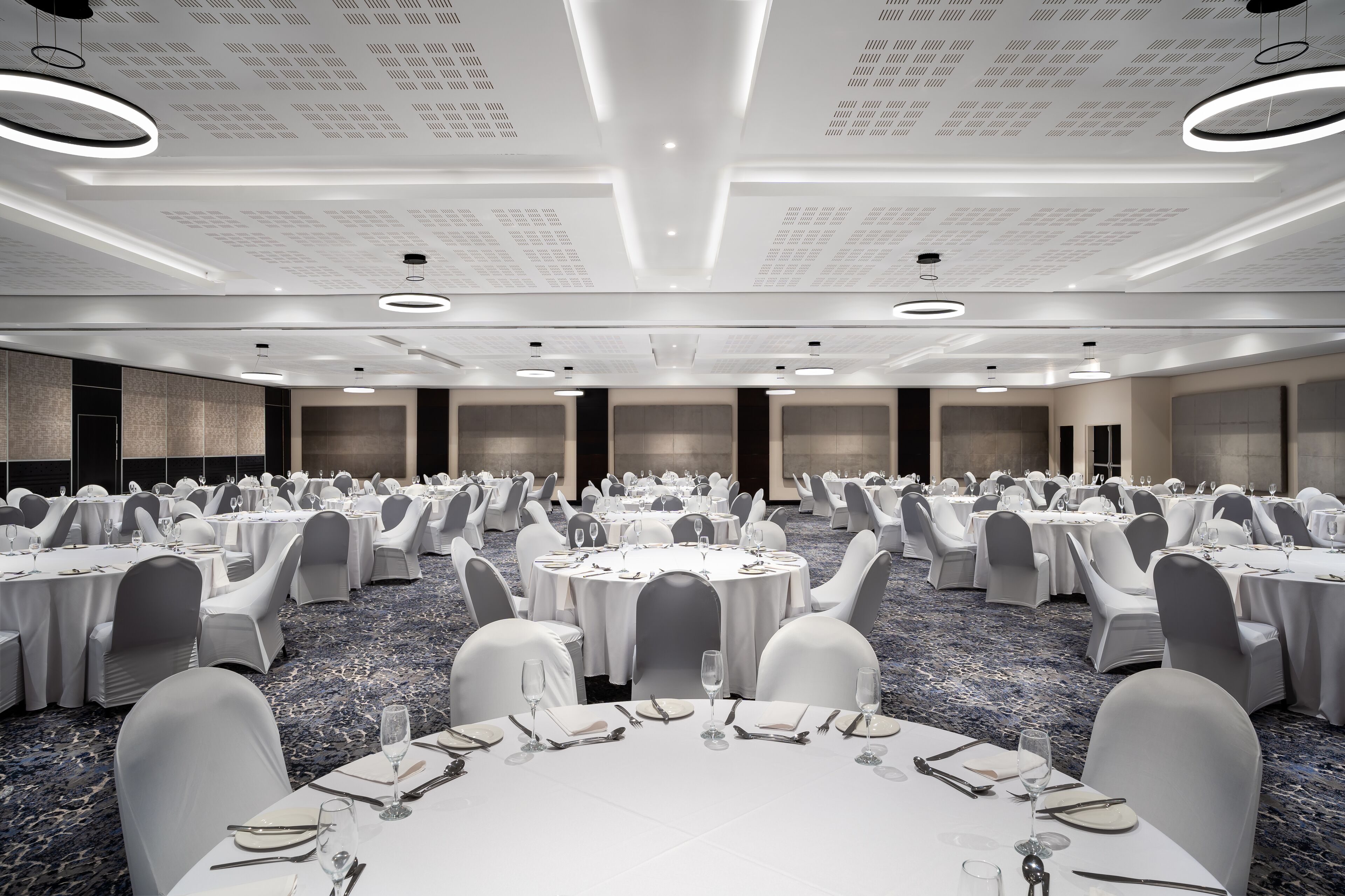 A large banquet hall with round tables, white tablecloths, and grey chairs.