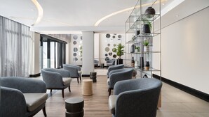 A modern lobby with grey upholstered chairs, a glass shelving unit with plants, and a curved ceiling design. - Premier Splendid Inn Umhlanga (Umhlanga)