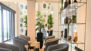 A modern waiting area with grey upholstered chairs, a central plant, and a glass display shelf with decorative items. - Premier Splendid Inn Umhlanga (Umhlanga)