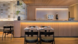 A modern restaurant with a wooden panel wall, a glass display case with plants, and a bar area with a coffee machine. - Premier Splendid Inn Umhlanga (Umhlanga)