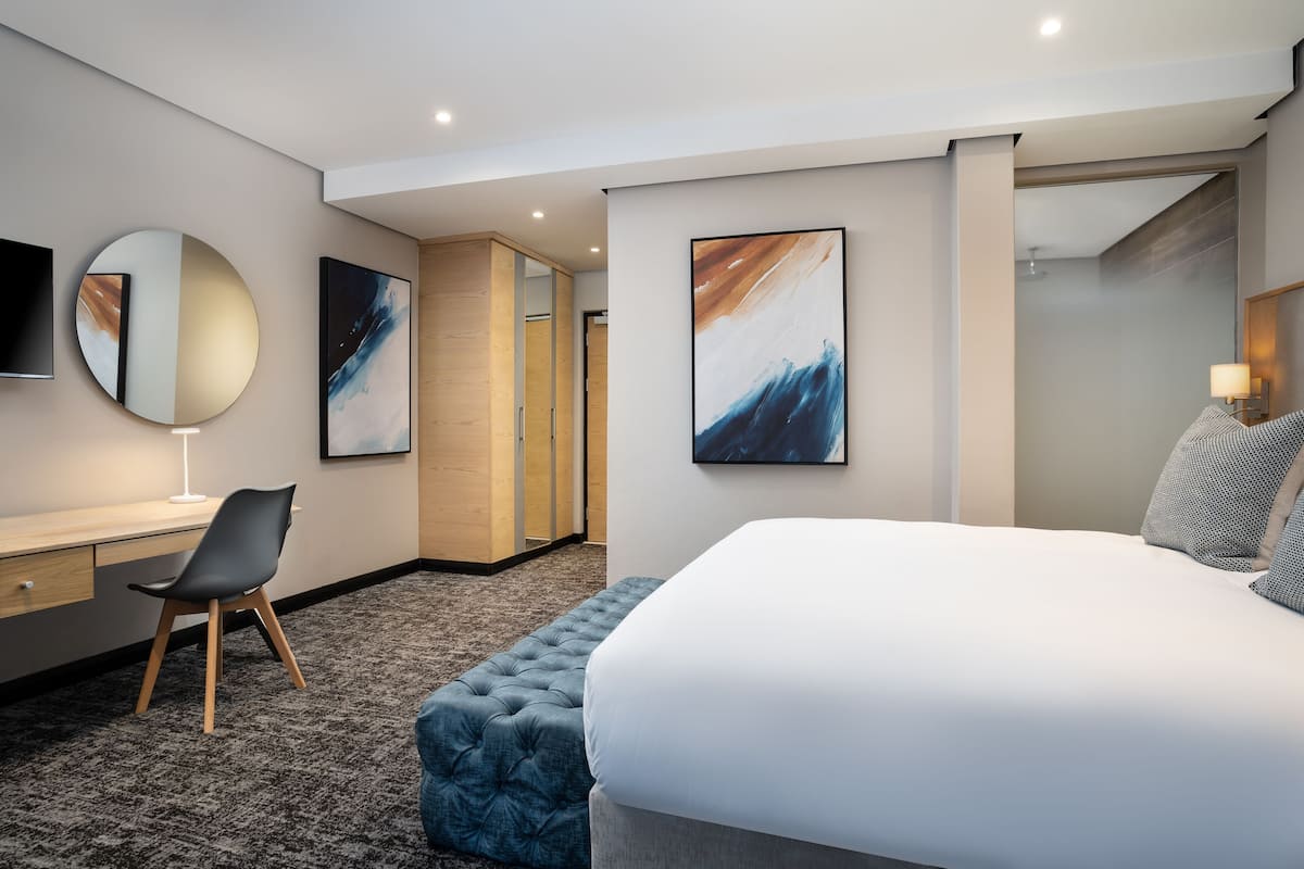 A modern hotel room with a large bed, a desk, a chair, and artwork on the walls.