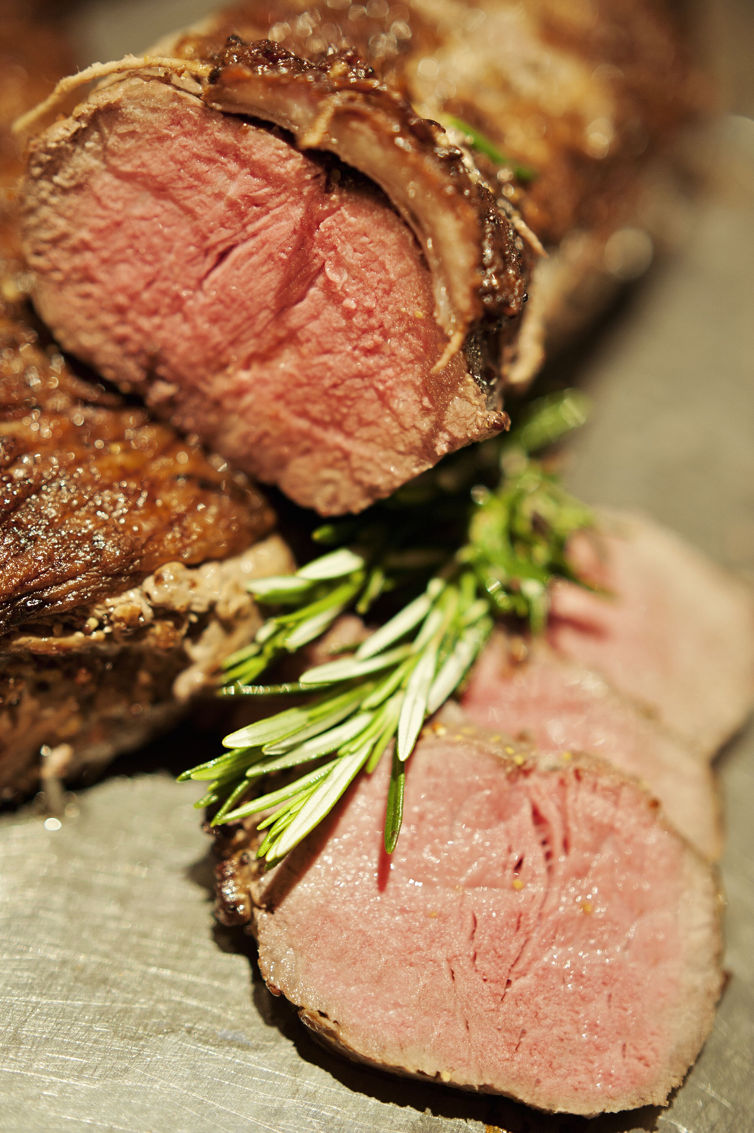 A close-up of a cooked meat dish with a slice cut out, garnished with rosemary.