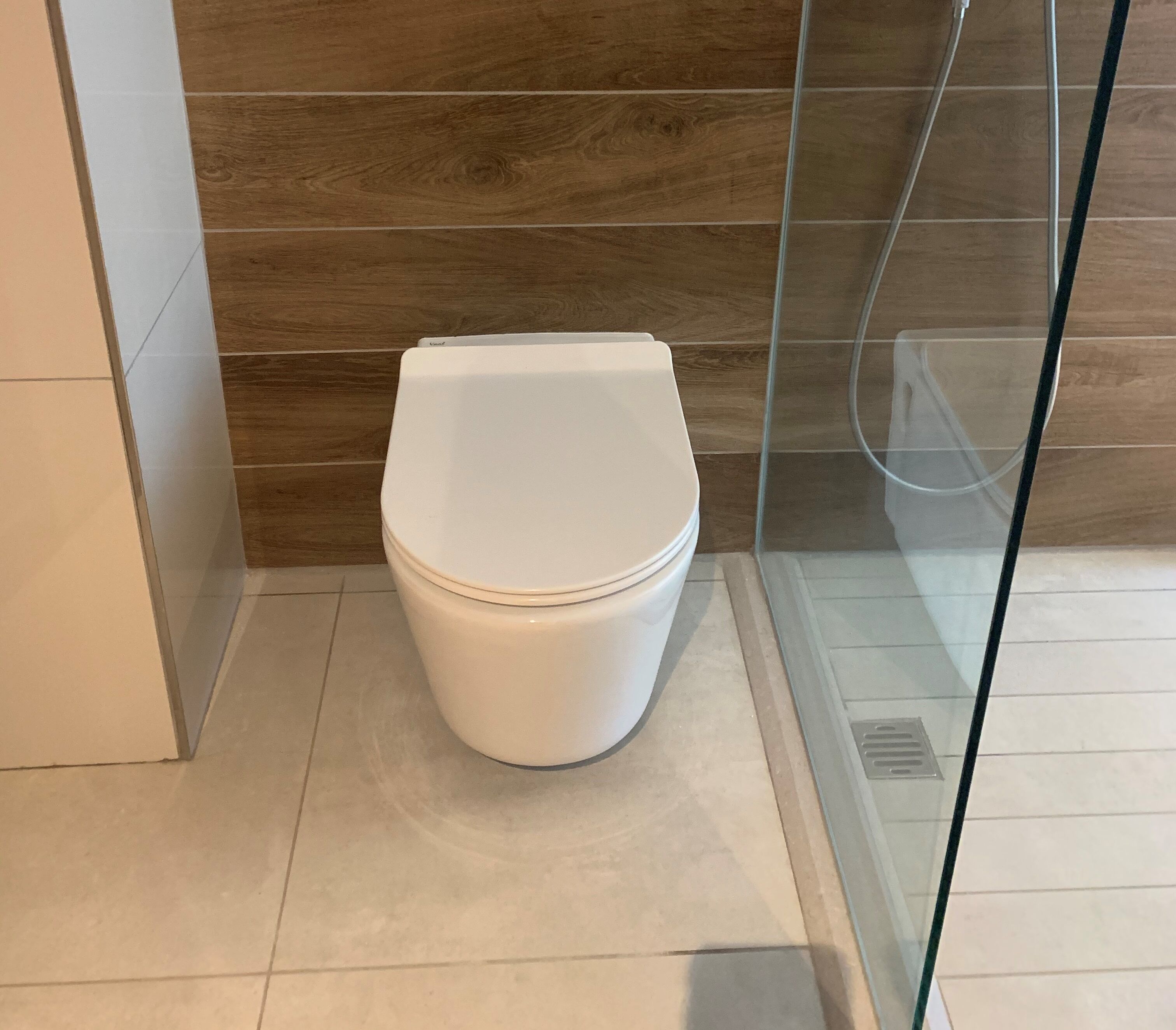 A modern bathroom with a white toilet, wooden wall paneling, and a glass shower enclosure.