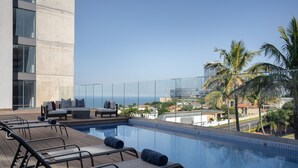 A rooftop pool with lounge chairs and a sofa, overlooking a cityscape and palm trees. - Premier Splendid Inn Umhlanga (Umhlanga)