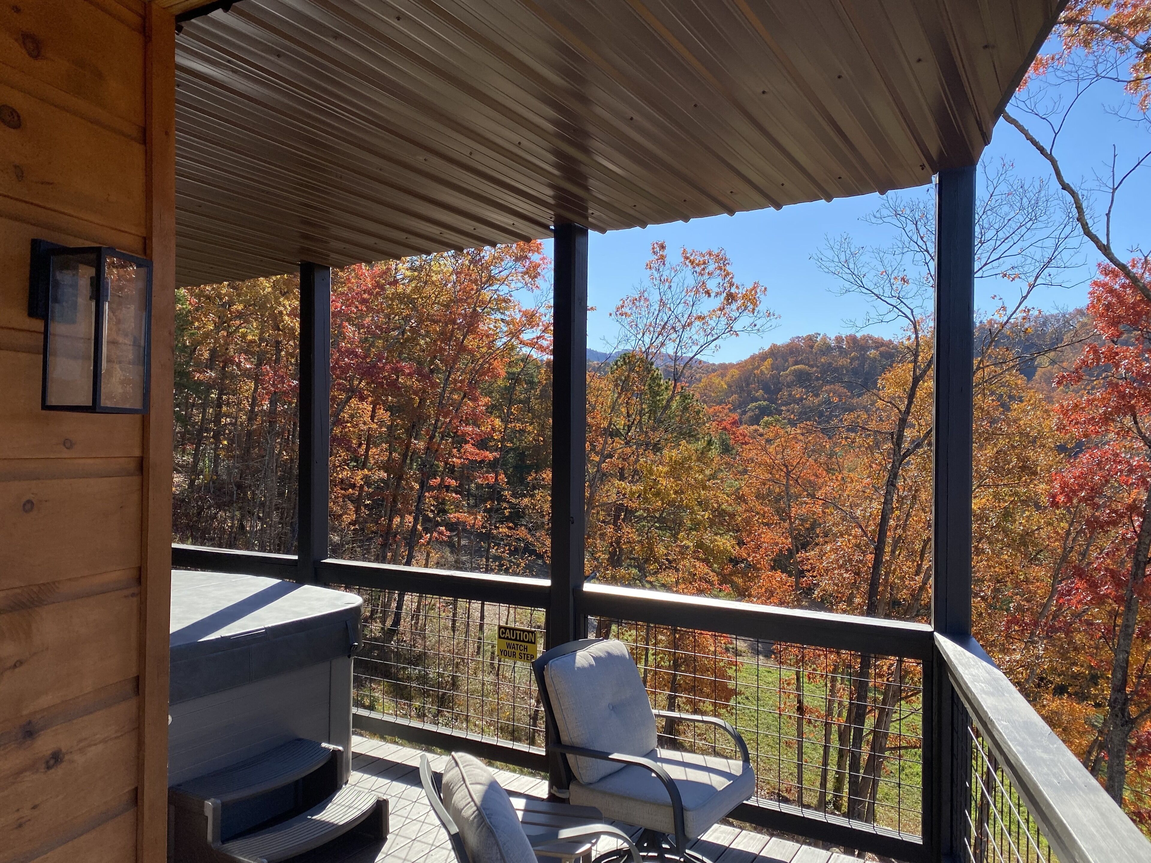 Une terrasse en bois avec un banc et une table, donnant sur une forêt aux couleurs automnales.