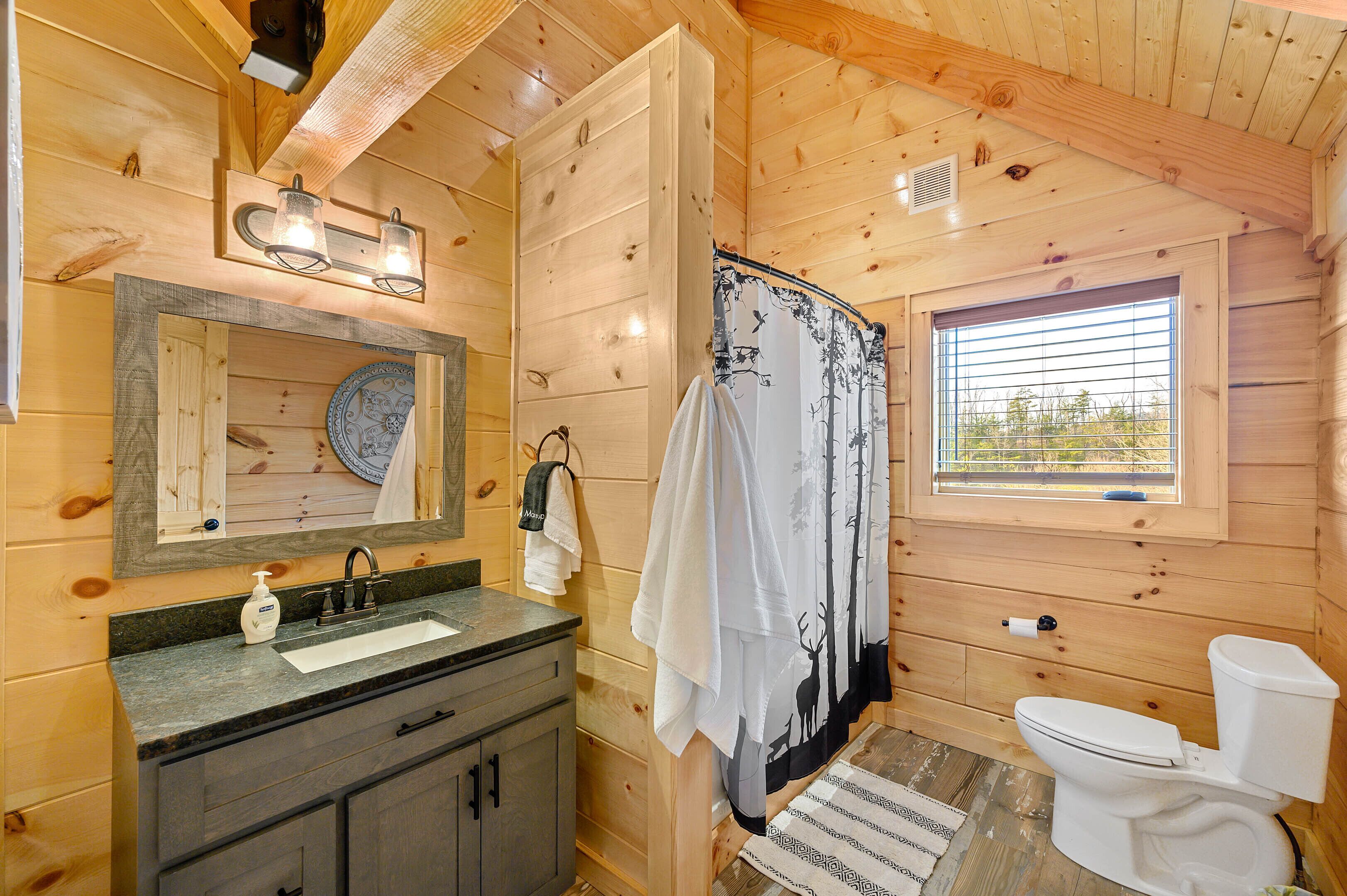 Een houten badkamer met een wastafel, spiegel, douchegordijn en toilet.