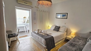 A hotel room with a bed, bedside table, lamp, and a view of the balcony. - Room-pleasure Room 2 By The Sea (Santorini)
