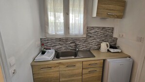 Eine kompakte Küche mit Spüle, Wasserkocher, kleinem Kühlschrank und Mikrowelle. Holzschränke und eine geflieste Spritzschutzleiste sorgen für eine gemütliche Atmosphäre.