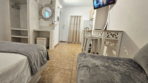 Habitación de hotel con dos camas, un televisor montado en la pared, un espejo y una pequeña zona de estar.