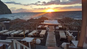 Zona de descanso junto a la playa con tumbonas y sombrillas de paja, con vista al océano al atardecer.