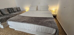 A bedroom with a large bed, a sofa, two bedside lamps, and a patterned pillow. - Room in Studio - Pleasure Room 4 By The Sea (Santorini)