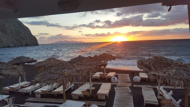 Vista de la playa con un atardecer, sillones de descanso y sombrillas de paja.