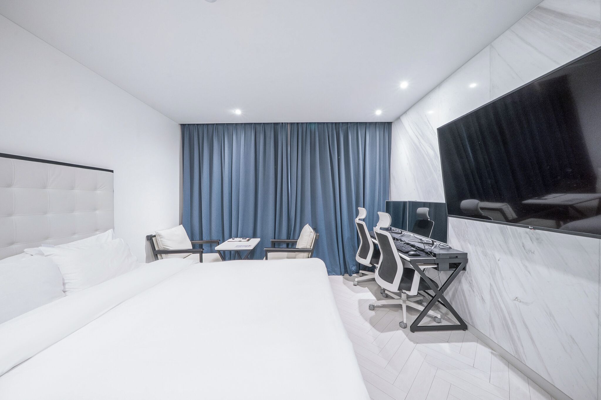 Una habitación de hotel moderna con una cama grande, un escritorio con dos sillas, un televisor de pantalla plana y un ventanal con cortinas.