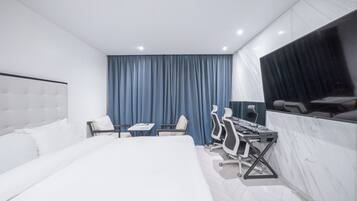 Una habitación de hotel moderna con una cama grande, un escritorio con dos sillas, un televisor de pantalla plana y un ventanal con cortinas.
