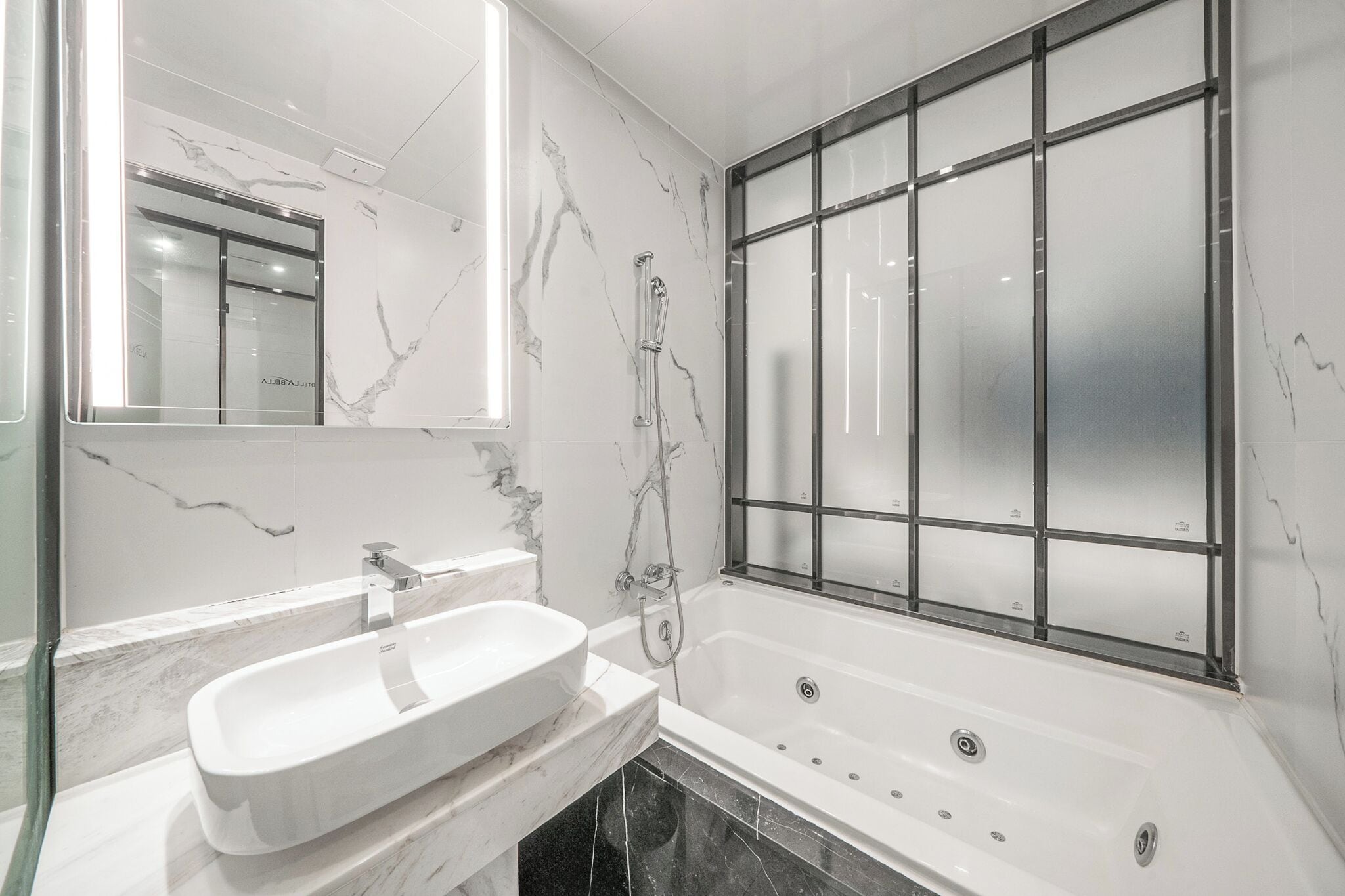A modern bathroom with a marble vanity, a bathtub with a glass enclosure, and a large mirror.