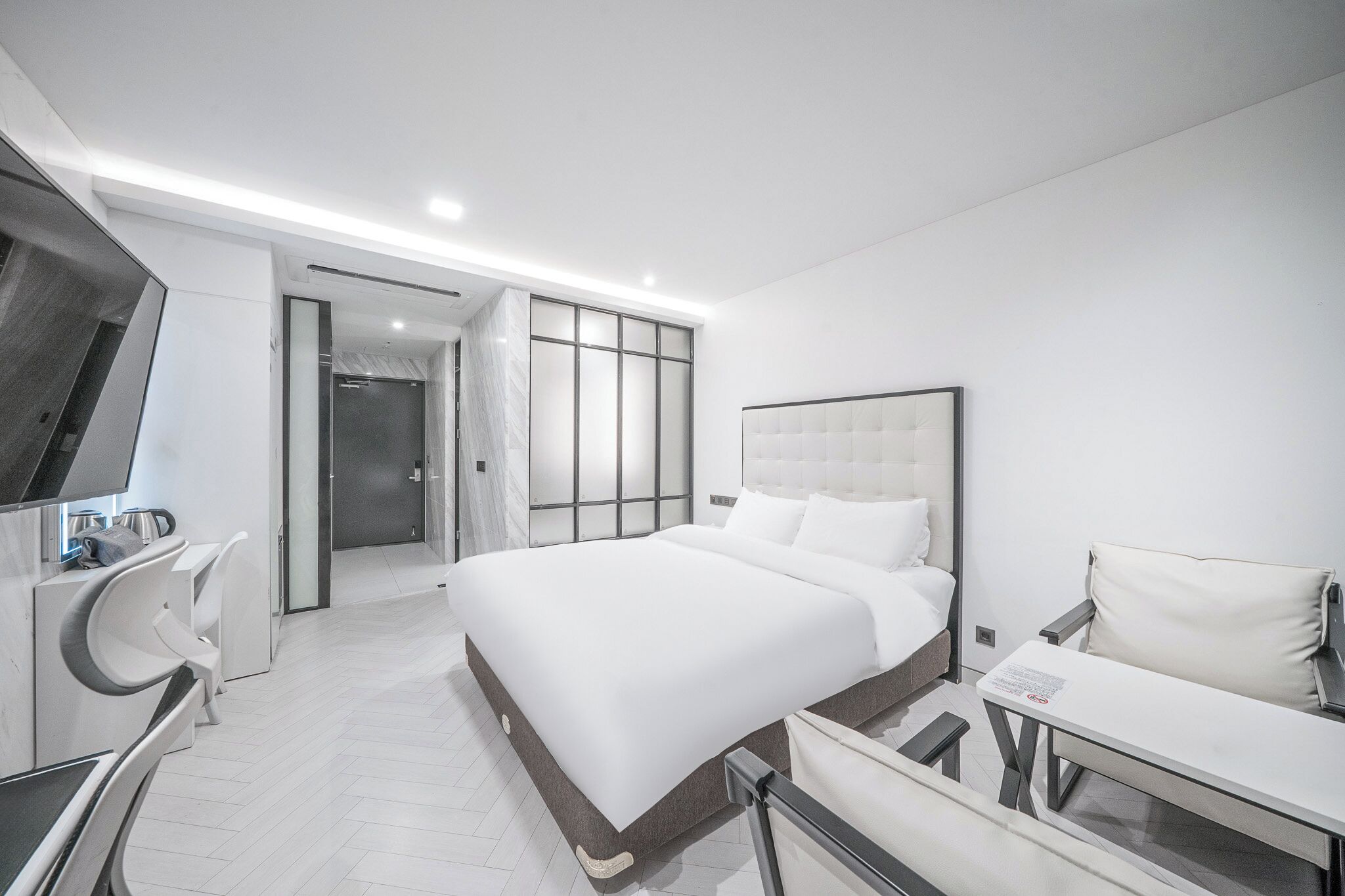A modern hotel room with a large bed, a desk, a chair, and a TV.